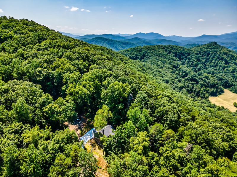Summer aerial view over the wooded hillside toward the Smoky Mountains, the cabin roof among the trees