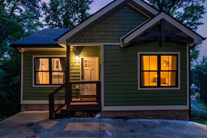 Front of the green craftsman cabin at twilight, porch light on and warm light in the windows
