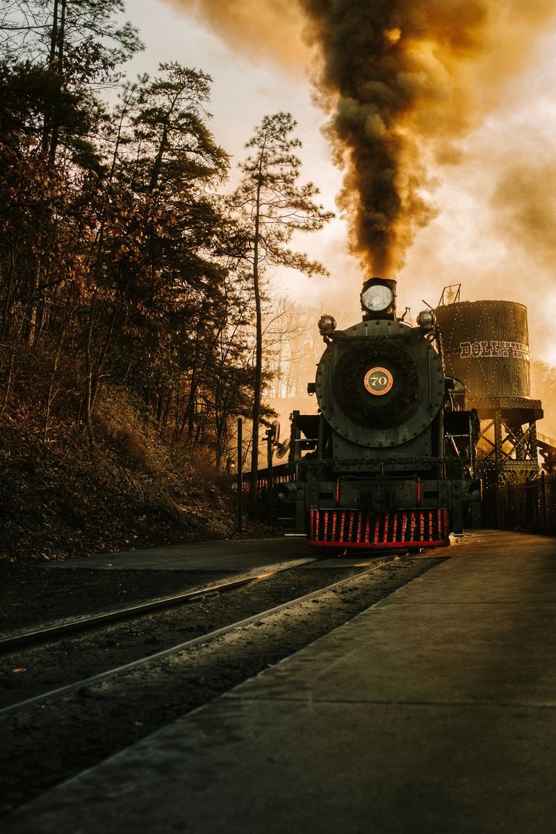 Dollywood's steam locomotive No. 70, dressed with a holiday wreath, under a plume of smoke at sunset beside a lit water tower