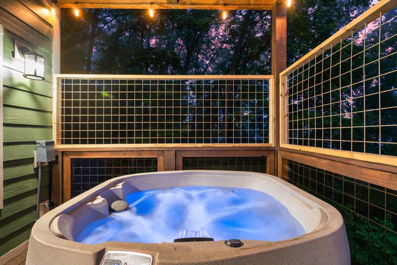 Lit hot tub on the covered lower deck under string lights