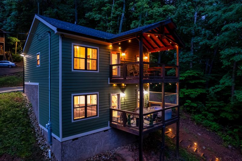 The cabin at dusk from above, both covered decks lit with string lights among tall trees