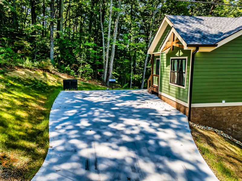 The short, steep paved driveway climbing to the cabin's parking pad on a summer day