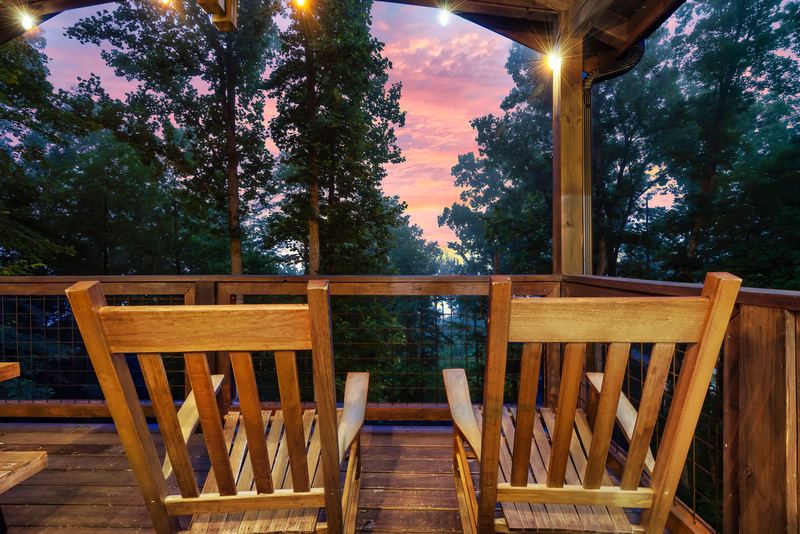 Two wooden rocking chairs on the upper deck facing the trees at sunset